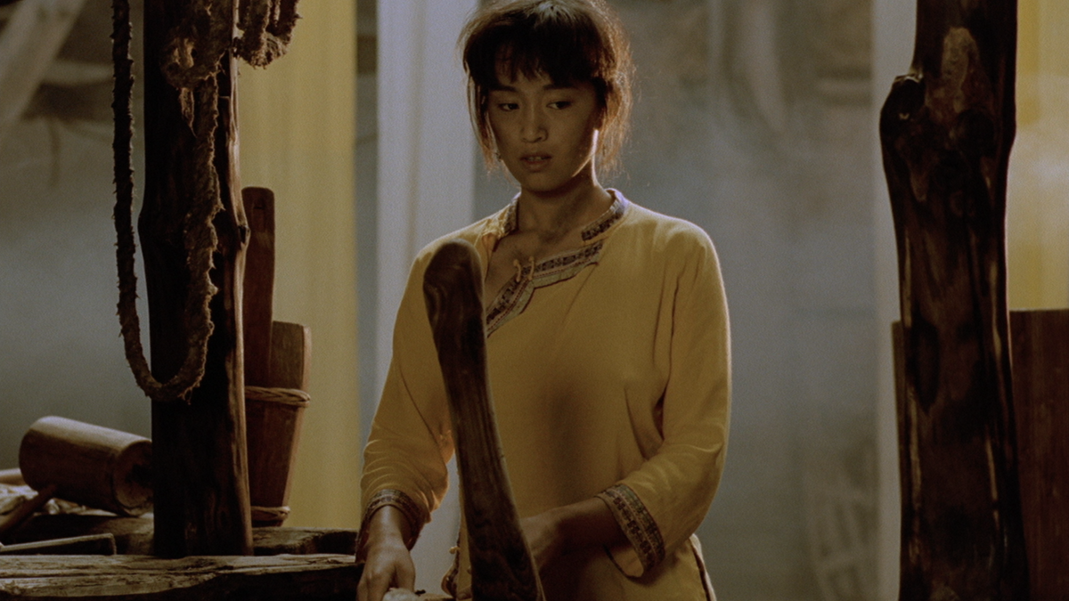 JU DOU, 1990, woman in yellow sweater holding long object looking down