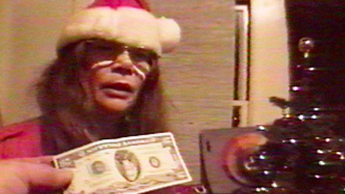 person wearing red santa hat holding out a dollar bill in living room