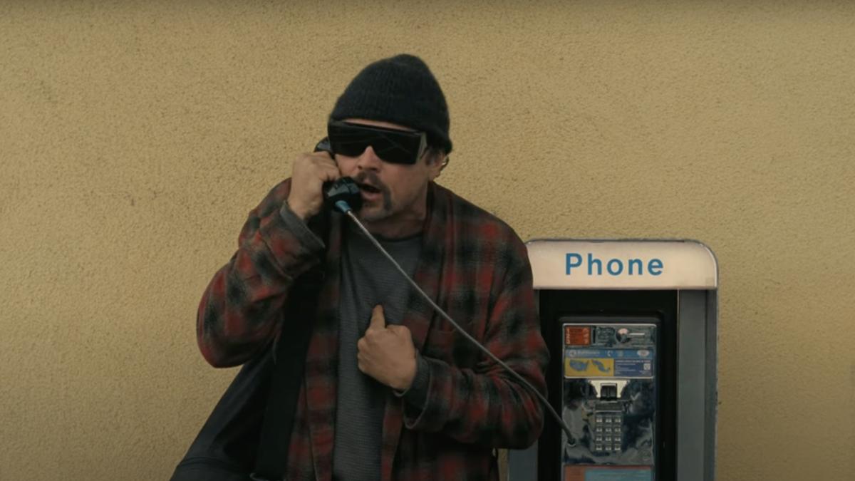 ONE BATTLE AFTER ANOTHER, 2025, man in plaid robe, sunglasses, and beanie talking on pay phone