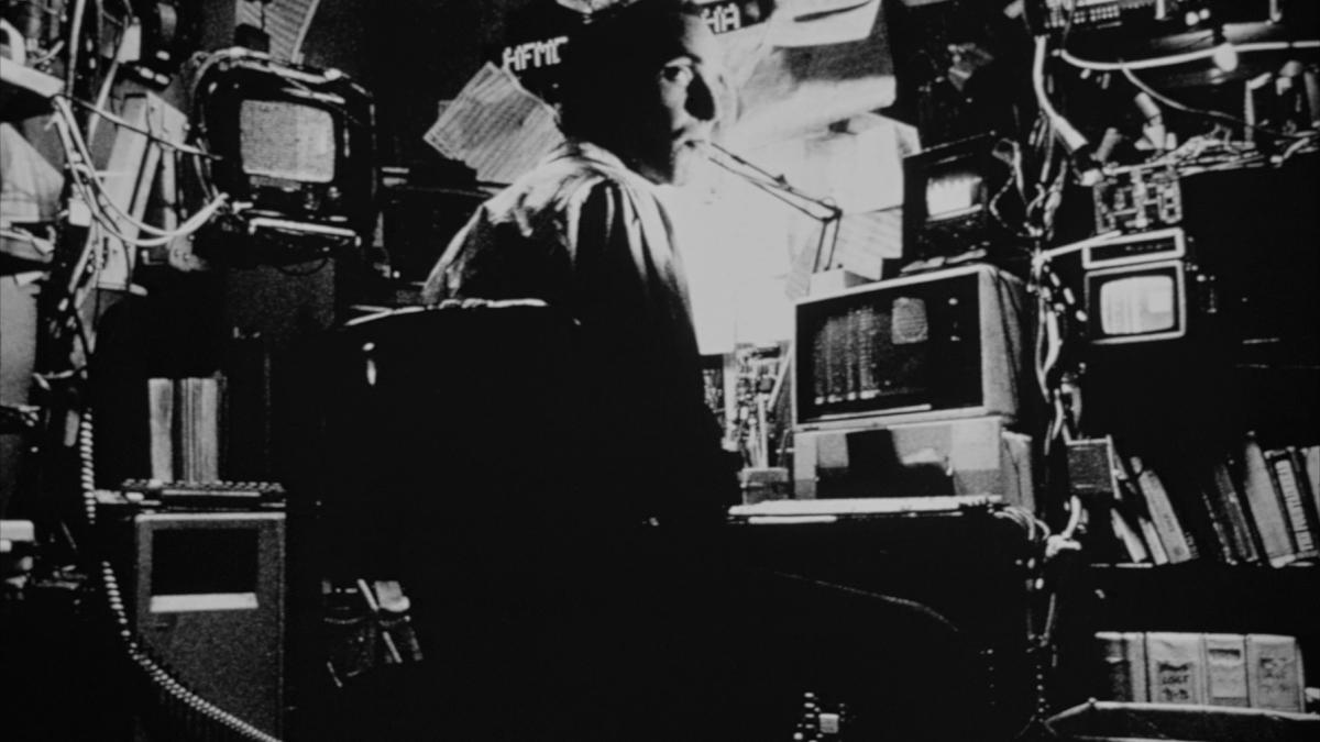 PI, 1998, black and white still of man seated at cluttered computer desk turning around in chair 