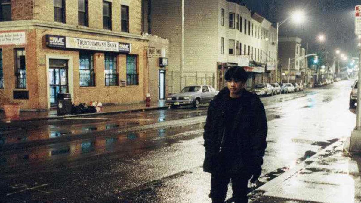BATANG WEST SIDE, 2001, man in winter coat walking on sidewalk along wet empty street