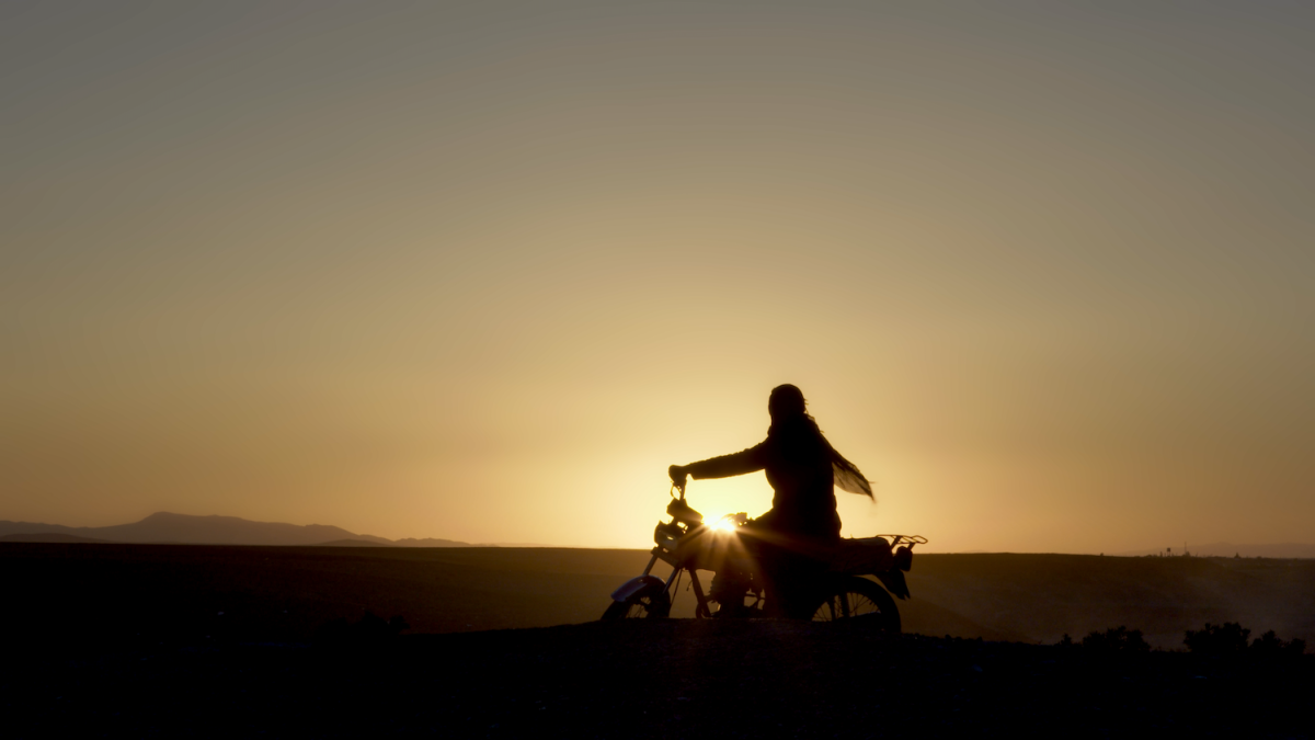CUTTING THROUGH ROCKS, 2025, silhouette of a person on motorcycle in front of sunset and vast landscape