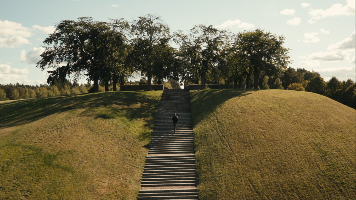 LEWERENTZ DIVINE DARKNESS, 2025, man climbing set of stairs leading to the top of a large grassy hill