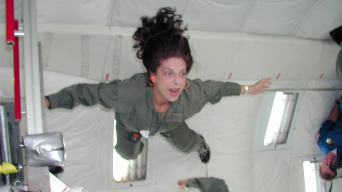 THE SPACE ARCHITECT, 2025, woman in outer space holding arms outstretched in zero gravity