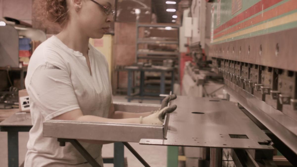 PARK LANES, 2015, woman in white shirt and ponytail working in factory and wearing gloves