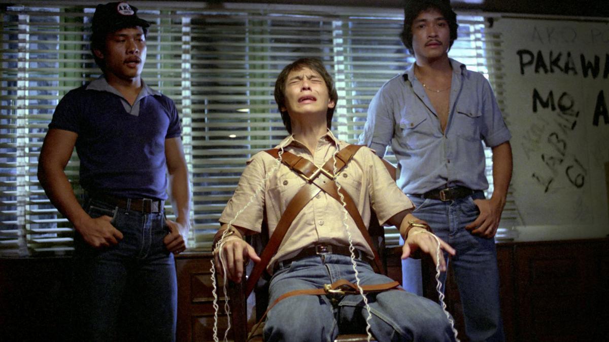 BATCH '81, 1982, man strapped to a chair with two men standing behind him in dimly lit room