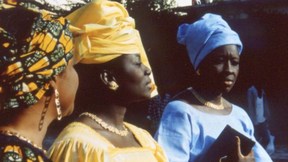 FAAT KINE, 2000, three woman in colorful dresses and head scarfs seated in a row next to each other