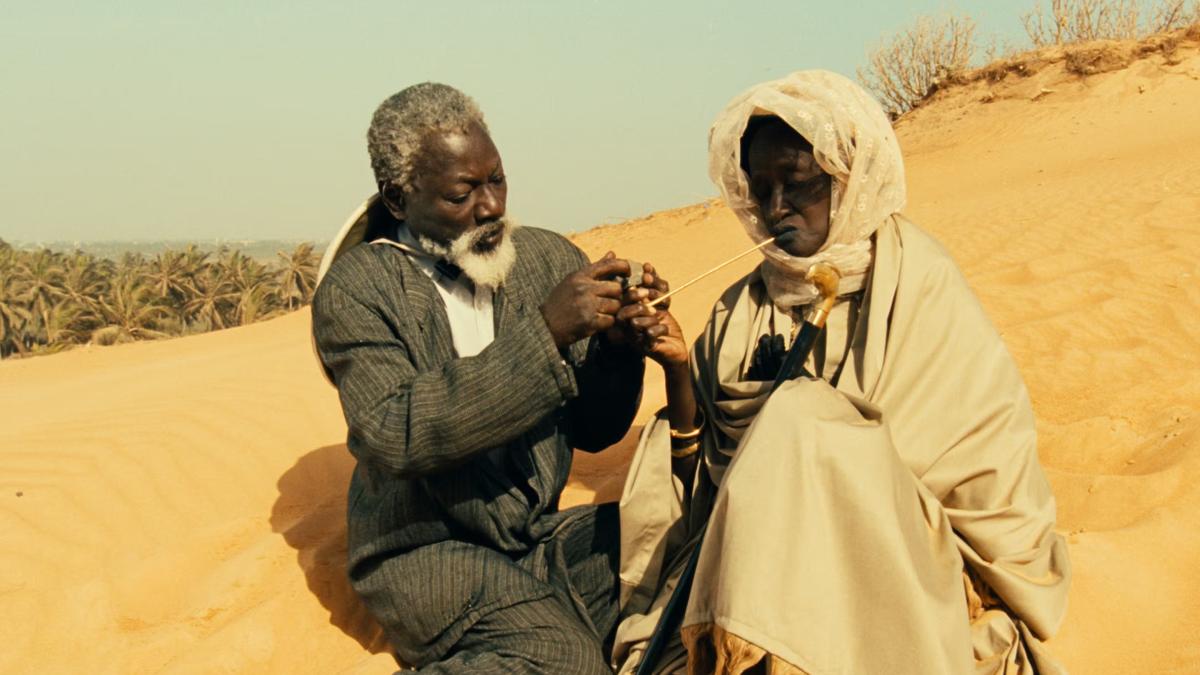 HYENAS, 1992, elderly man in suit seated next to woman in the desert