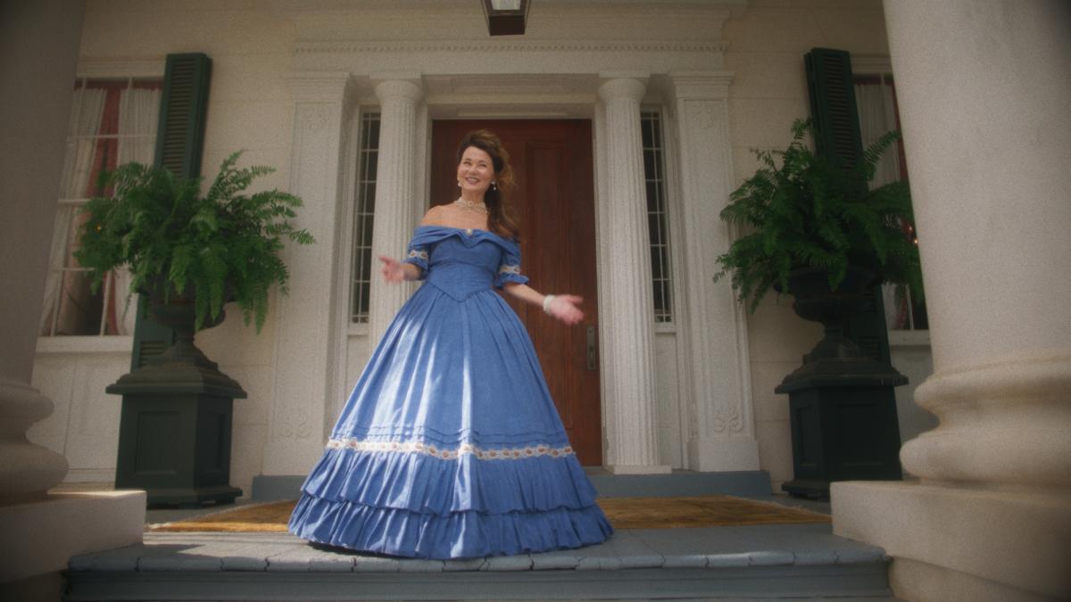 NATCHEZ, 2025, woman in blue corset dress standing on front porch of house with arms out to side