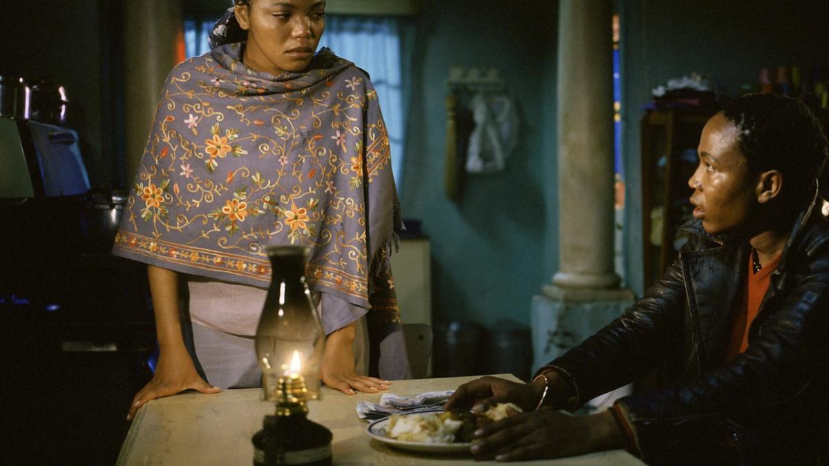 TSOTSI, 2005, man seated with food at table with woman standing on table looking at him