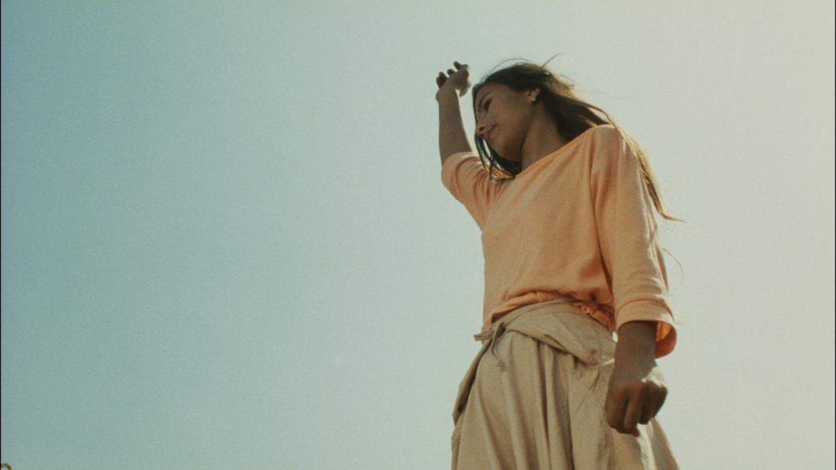 THE RAZOR'S EDGE, 1985, worm's eye view of woman standing up holding fist in air outside