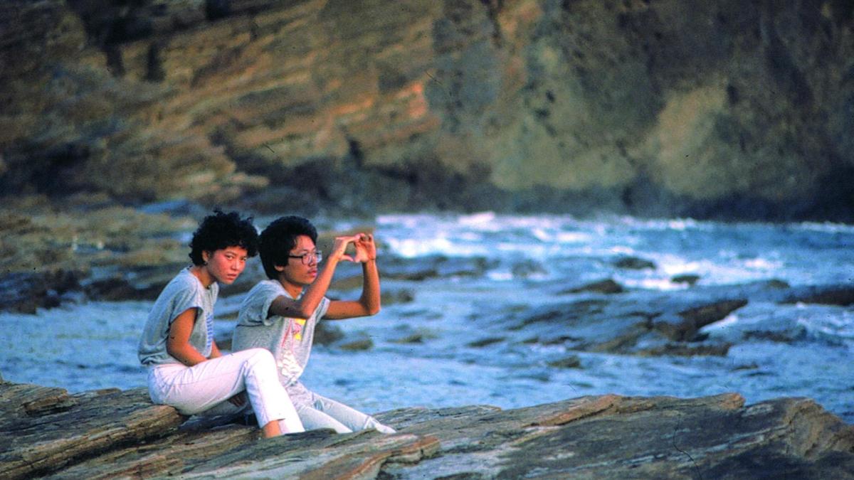 AH YING, 1983, Asian couple seated on rock near water with man holding out hands 
