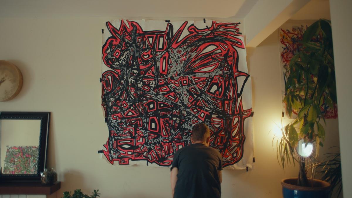 AMANDA, 2025, multimaterial, three-dimensional art hanging on wall with man standing in front of it looking