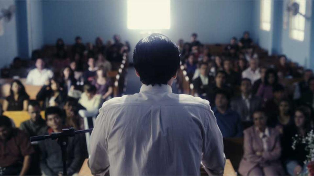 Back of man's head standing at podium in front of large crowd