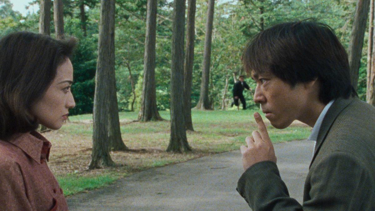 SERPENT'S PATH, 1998, man and woman facing each other in a park with man holding one finger to his lips