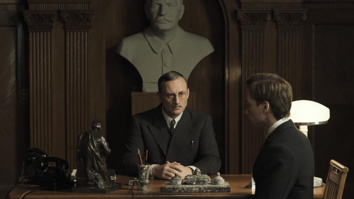 TWO PROSECUTORS, 2025, two men sitting across office desk with large bust behind them