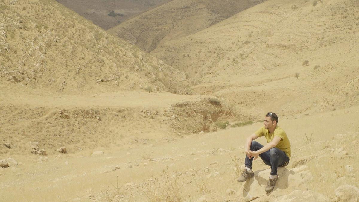 HOLIDAYS IN PALESTINE, 2024, man sitting in vast desert on ground with arms resting on his legs