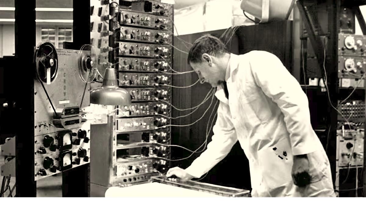 JOHN LILLY AND THE EARTH COINCIDENCE CONTROL OFFICE, 2025, black and white image of man in lab coat working on large wall of technology