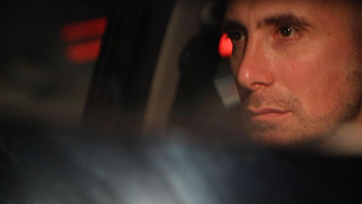 WHO KILLED ALEX ODEH?, 2025, close up of man's face in right side of frame riding in car