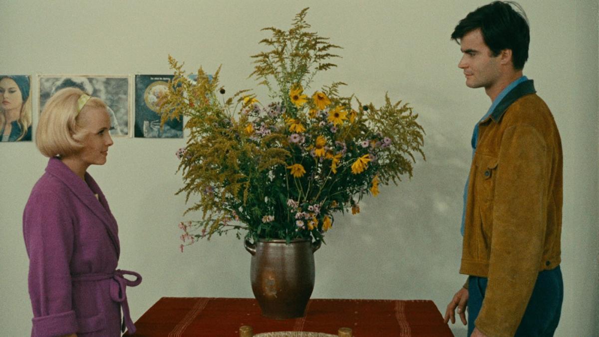 LE BONHEUR, 1965, couple standing across from each other at table with large vase of flowers in the center of table