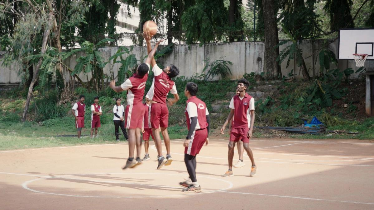 HOOP LIKE THIS, 2025, group of young boys playing basketball on outdoor court with matching red uniforms
