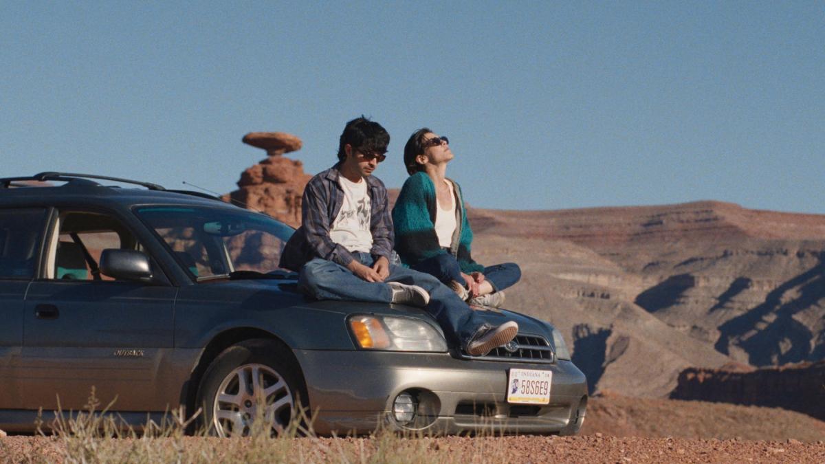 HOT WATER, 2025, couple sitting on hood of car in desert looking into distance