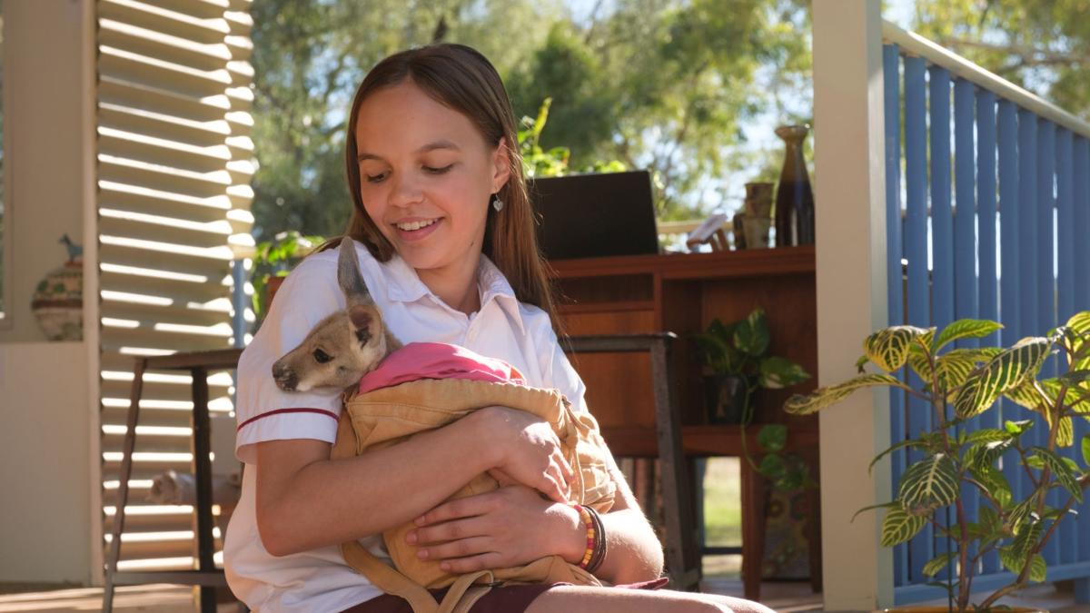 KANGAROO, 2025, young girl sitting on porch holding a baby joey kangaroo