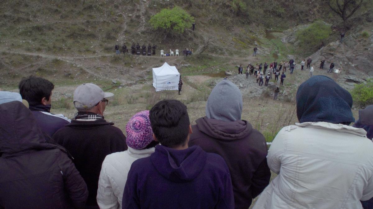 OUR LAND, 2025, group of people in jackets and hats looking down hill at a tent in the grass