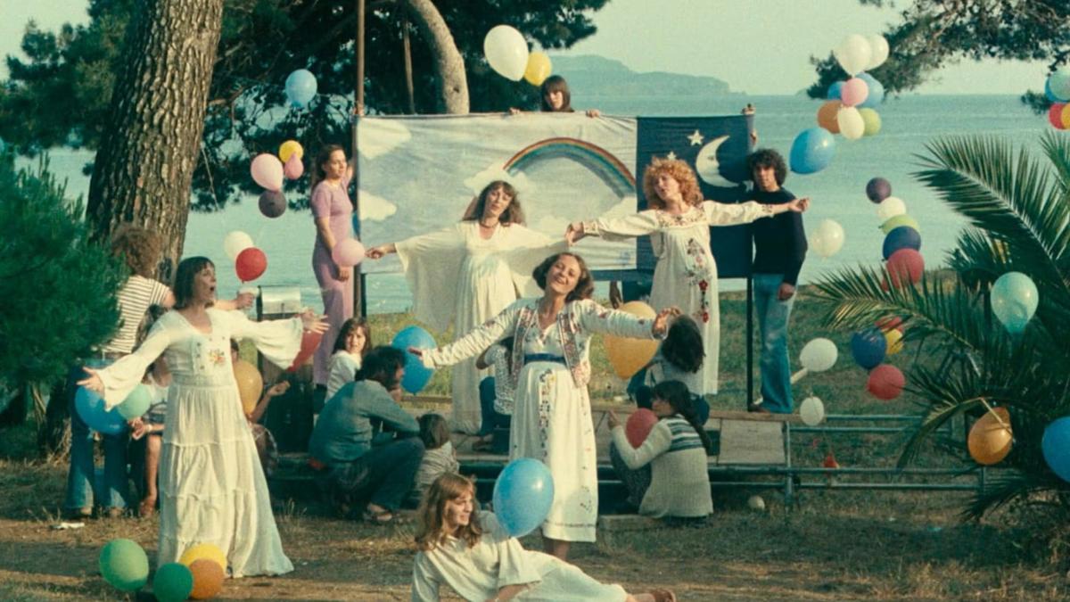 ONE SINGS THE OTHER DOESN’T, 1977, group of several women in long white dresses performing outside with lots of festive balloons and decorations around