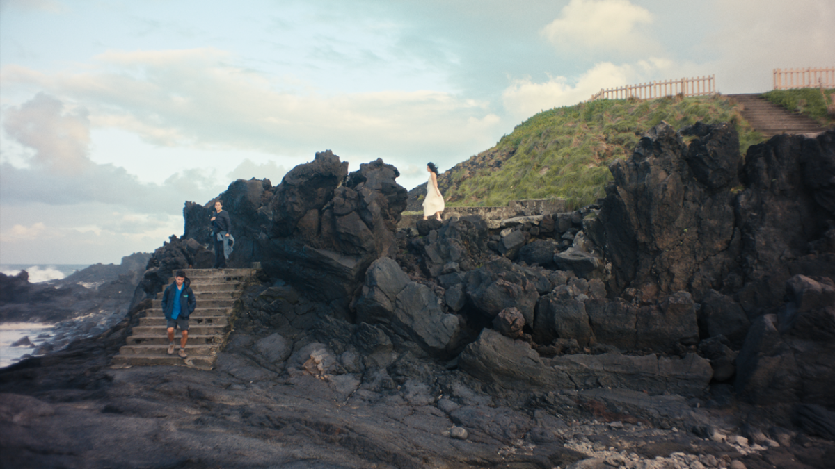 HONEYJOON, 2025, rocky cliff overlooking ocean with three people making way down steps closer to ocean