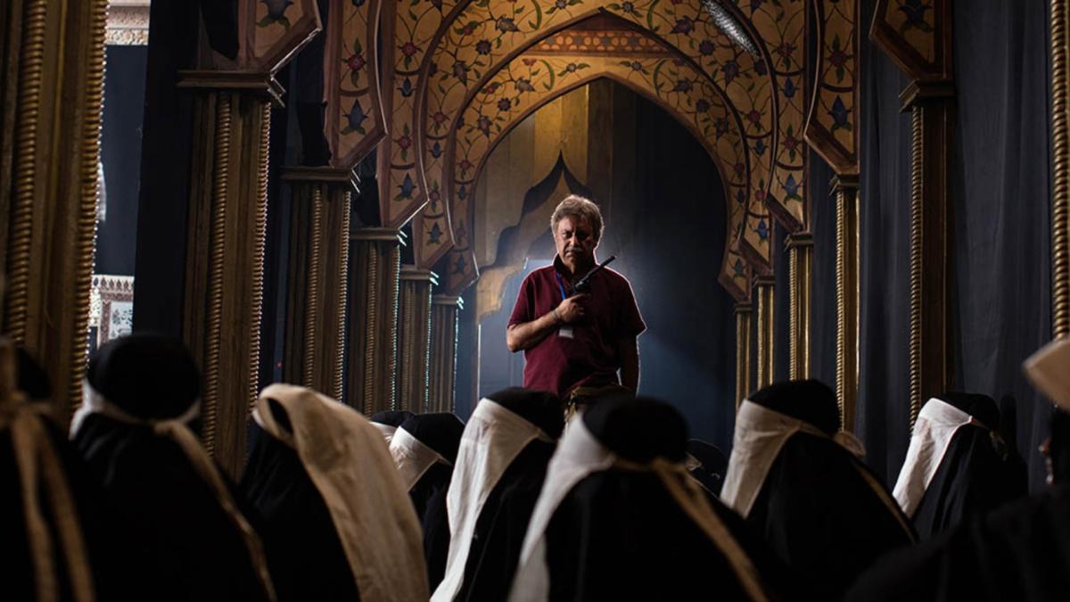 BLACK RABBIT WHITE RABBIT, 2025, man standing in front of seated group inside large house of worship