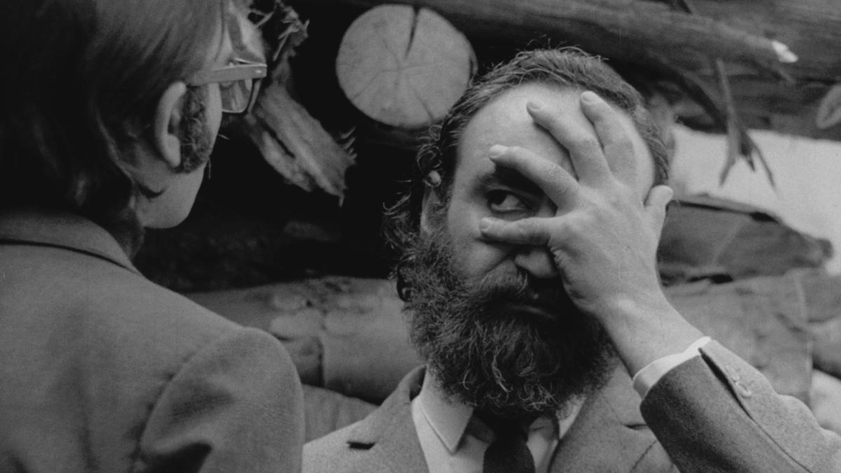 DOWNPOUR, 1972, black and white image of man with hand on his face and eye peeking between fingers at man across from him