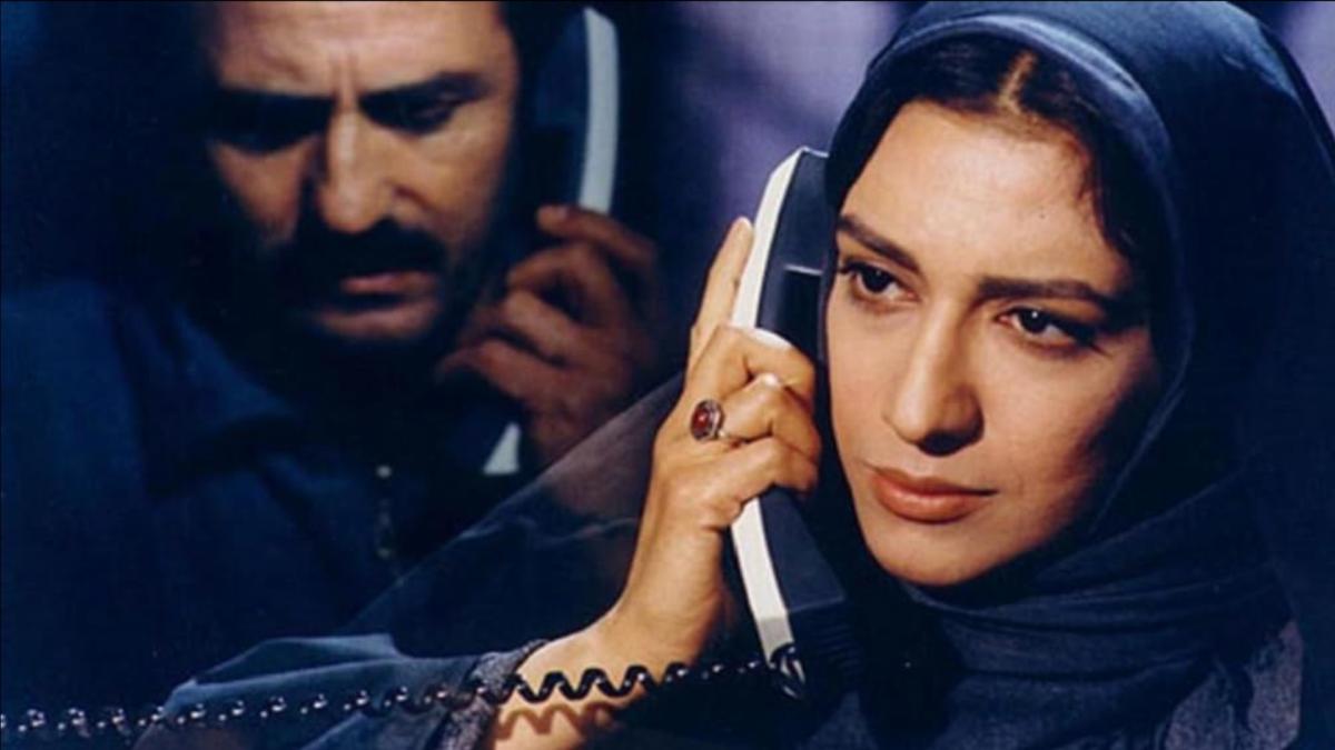 KILLING MAD DOGS, 2001, woman wearing hijab holding phone up to ear with man in background holding phone up to his ear