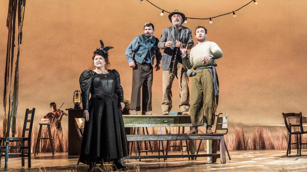 NATIONAL THEATRE LIVE: THE PLAYBOY OF THE WESTERN WORLD, 2026, four people on stage looking out into distance with three men standing on wooden picnic table 