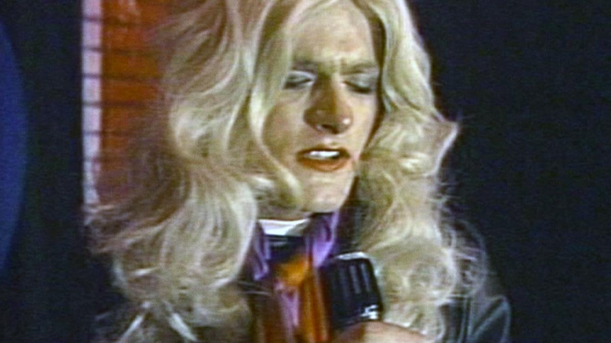 THE BEAVER TRILOGY, 2000, drag performer wearing blonde wig and holding microphone with eyes closed