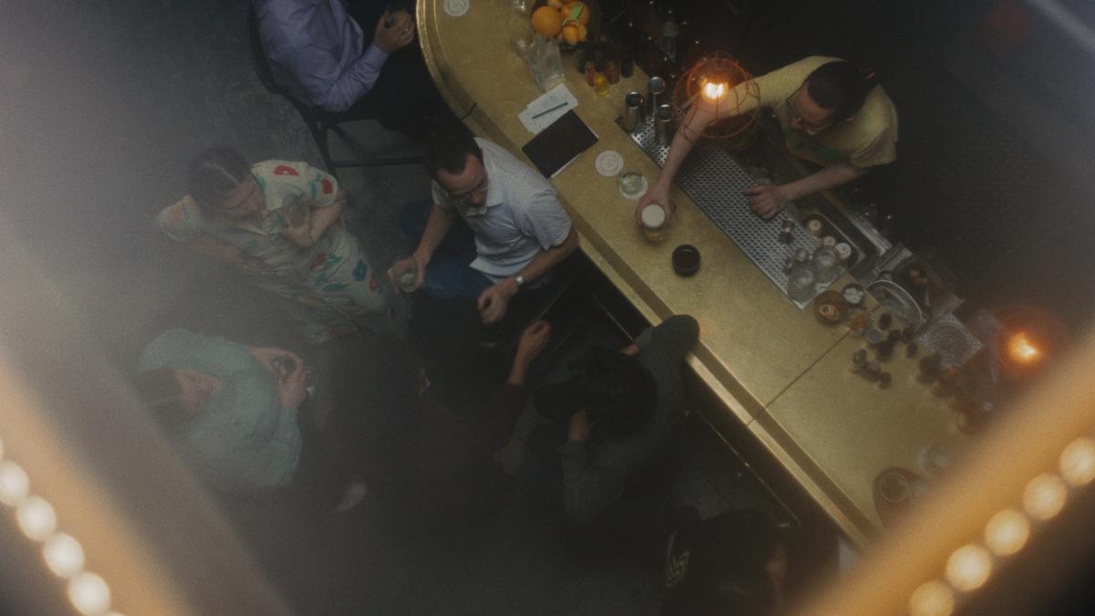 THE SCOUT, 2026, birdseye view of group of people talking, holding drinks, with lights above
