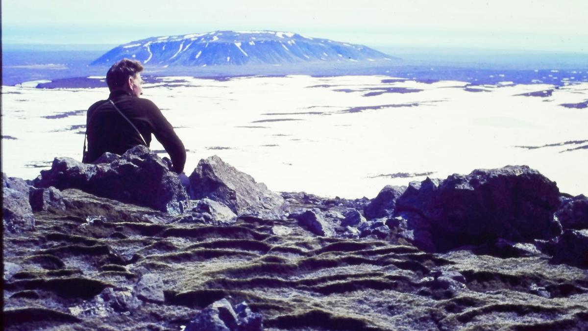 TIME AND WATER, 2026, person seated on edge of rocks looking out at ocean