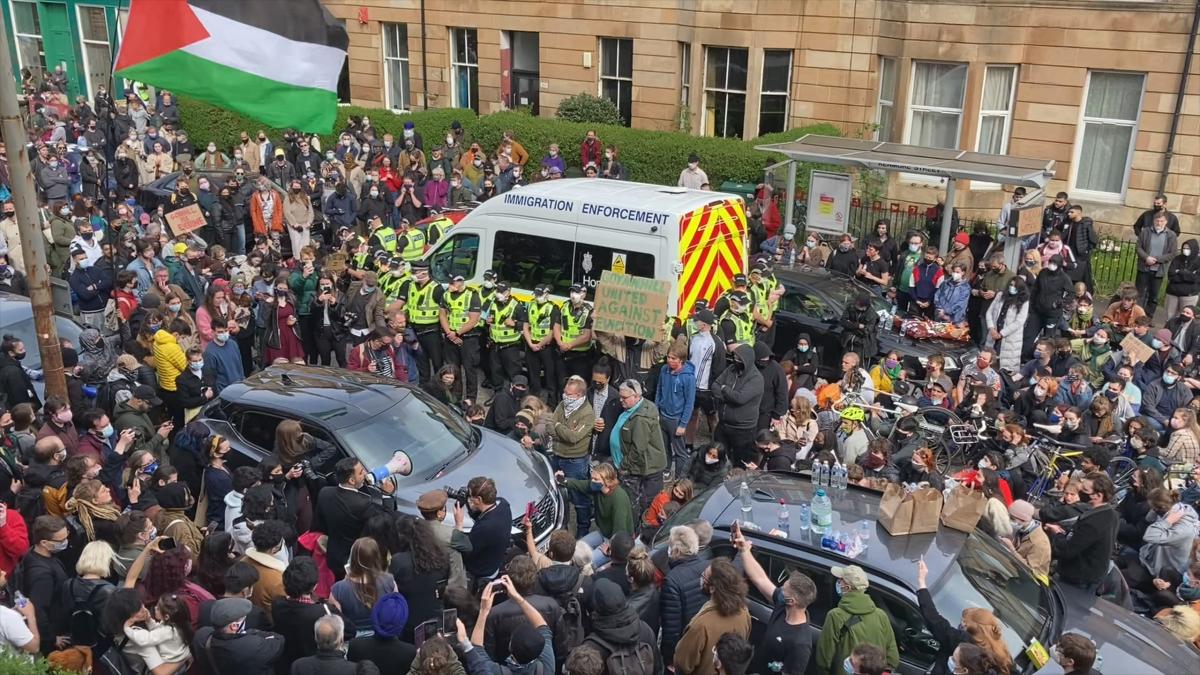 EVERYBODY TO KENMURE STREET, 2025, overhead shot of crowded street full of protesters and law enforcement van in the center of street