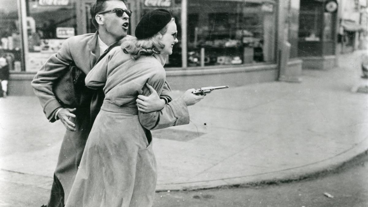 GUN CRAZY, 1949, man grabbing woman holding gun in fur coat and sunglasses through the street