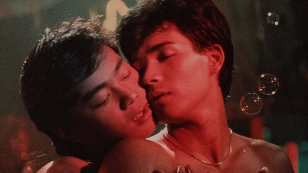 MACHO DANCER, 1988, two shirtless men holding each other with faces close at dimly lit club