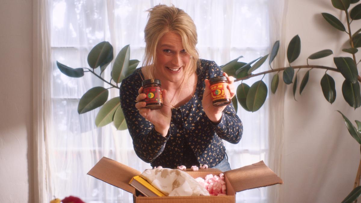 MADDIE'S SECRET, 2025, woman smiling and holding two jars over opened cardboard box in front of window