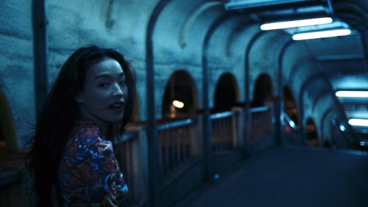 MILLENNIUM MAMBO, girl in dark outdoor concrete corridor turning around with slight smile