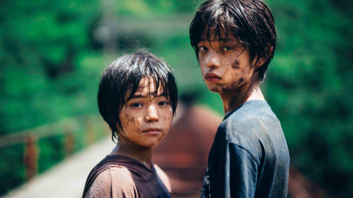 MONSTER, 2023, two young boys with dirt on faces looking back and standing onbridge outside