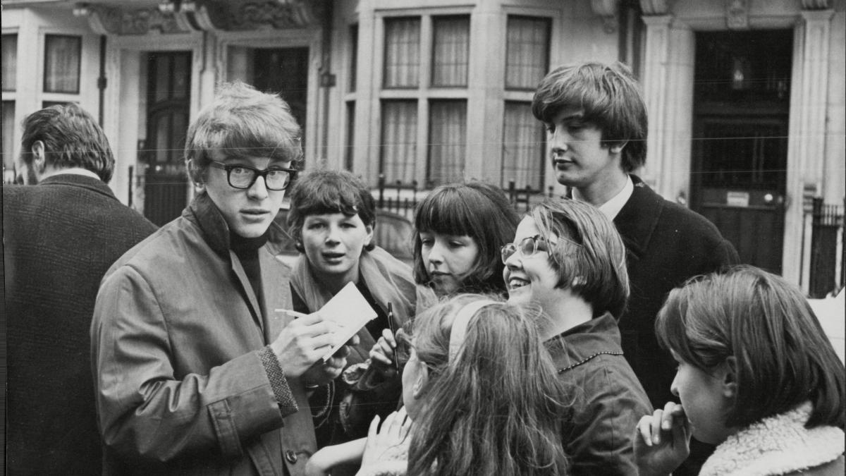 PETER ASHER: EVERYWHERE MAN, 2025, black and white image of man on the street with fans circling around him