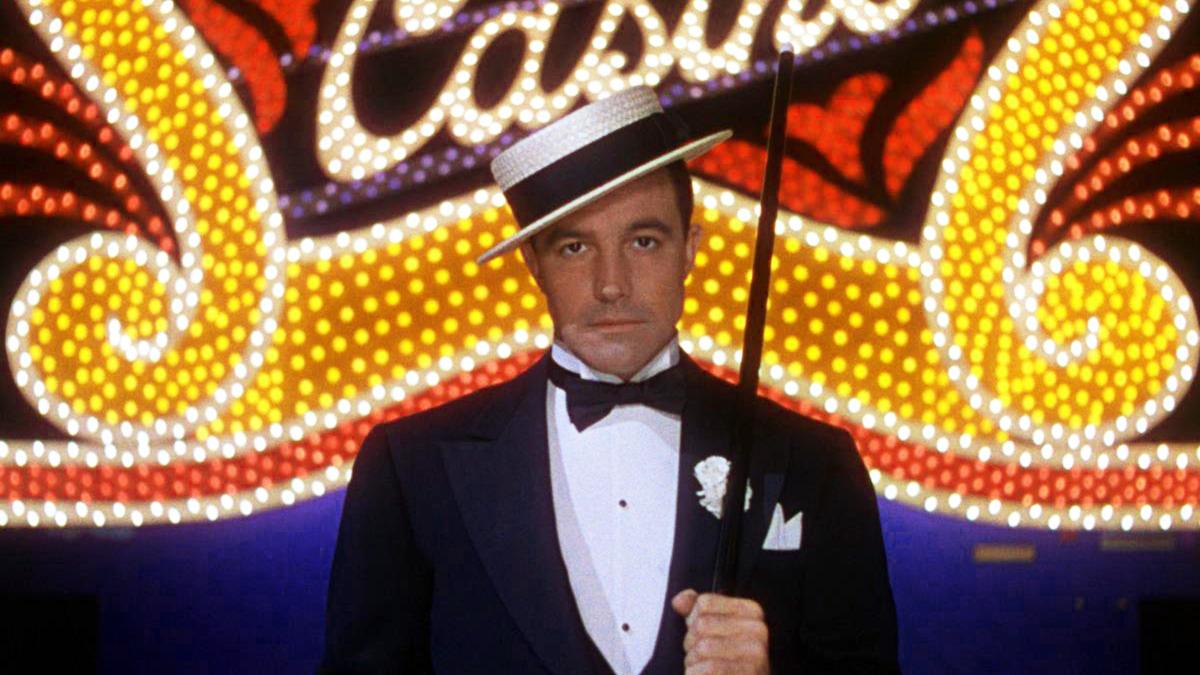 SINGIN' IN THE RAIN, 1952, man in suit and hat holding an umbrella in front of bright flashing neon sign that says "Casino"