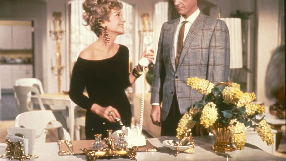 THE BUSY BODY, 1967, woman in a black dress and man in a plaid suit standing in kitchen over table with flowers