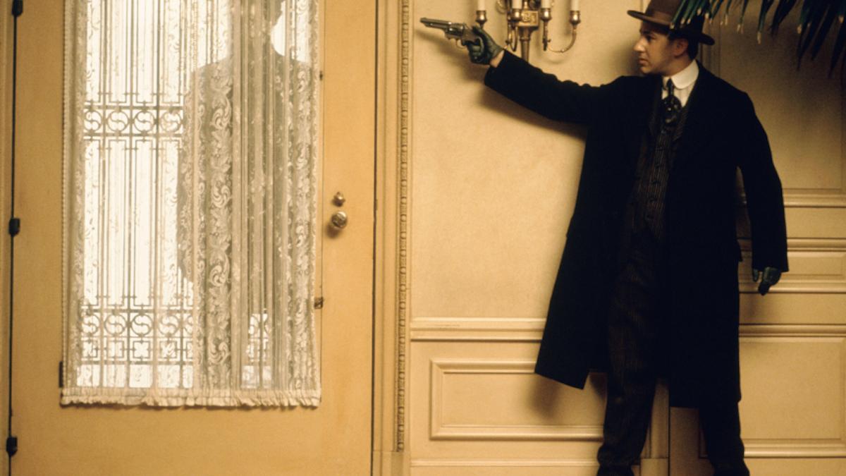 THE GODFATHER PART II, 1974, man in suit and hat standing behind door pointing gun with silhouette standing at door behind curtain