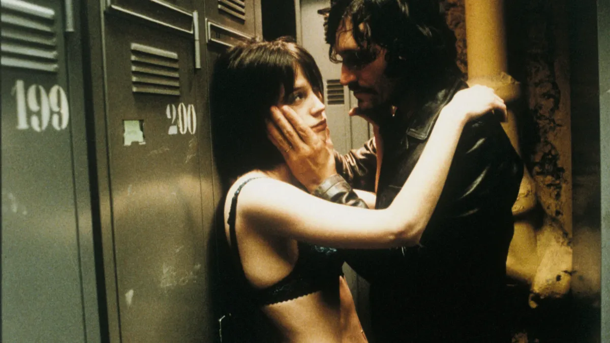 TROUBLE EVERY DAY, 2001, couple embracing each other against wall in dimly lit room