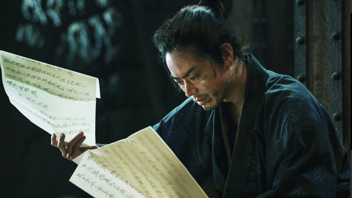 THE SAMURAI AND THE PRISONER, 2026, man in robe nad ponytail closely examining pieces of paper with handwriting on them