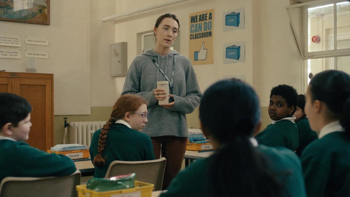 BAD APPLES, 2025, woman in sweater standing up and speaking to classroom of young students